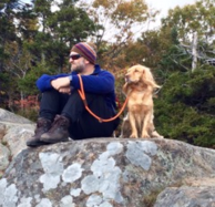 A man sitting on top of a rock with his dog.