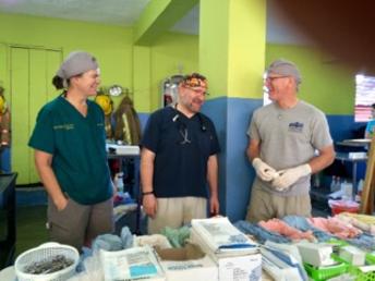 Three men standing in front of a table with many different items.