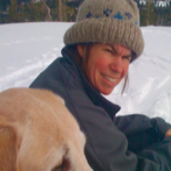 A woman and her dog are sitting in the snow.